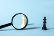 White chess queen, black chess queen and magnifying glass on a blue background. Abstract background. HR. Concept of search for new employees