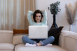 © alexfotobar - Young woman with computer and her arms crossed behind her head looking at the screen sitting at home on her sofa in the living room