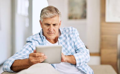 Poster - Scrolling through websites. Shot of a mature man using his digital tablet while relaxing on his sofa at home.