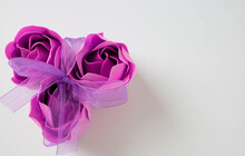 Three Pink Soap Roses Tied With A Lilac Ribbon On A White Background. Space For Text