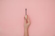 Woman hand holding an eyelash mascara on a pink background with copy space