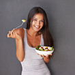 © Yuri Arcurs/peopleimages.com - A bowl of my best salad ingredients. Portrait of a healthy young woman eating a salad against a gray background.