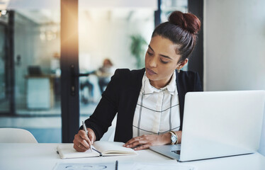 Wall Mural - Success is a consistent, daily effort. Shot of a young businesswoman making notes at her desk in a modern office.