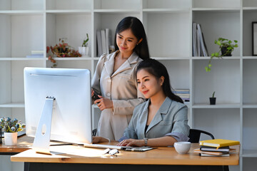 Wall Mural - Two successful businesswomen analyzing stock market on computer at bright workplace.