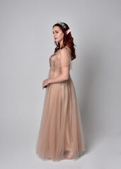 Poster - Full length portrait of pretty female model with red hair wearing glamorous fantasy tulle gown and crown.  Posing with gestural arms on a studio background