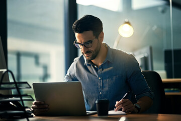 Canvas Print - Dedication makes all the difference. Shot of a young businessman using a laptop during a late night at work.