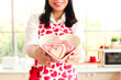 © Stella - ็Hands of happy smiling beautiful young Asian woman in cute red heart apron holding valentine homemade cookies, standing behind kitchen counter, prepare romantic love memorable anniversary celebration