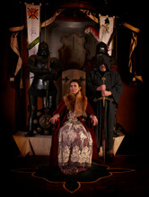 Medieval Countess (baroness, Princess, Queen) Sits On  Throne In  Ancient Castle. Behind Is  Monk-knight With  Sword. Historical Reconstruction, Beautiful Woman In St Miklos Castle In Ukraine