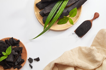 Wall Mural - Flatlay of bamboo activated charcoal and charcoal powder decorate with green leaf in white background 