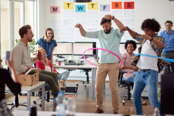 Wall Mural - Two male employees is playing with hula-hoop in the office with their colleagues. Employees, job, office