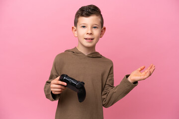 Wall Mural - Little caucasian boy playing with a video game controller isolated on pink background extending hands to the side for inviting to come