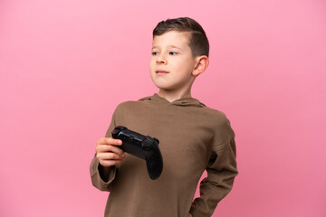 Wall Mural - Little caucasian boy playing with a video game controller isolated on pink background suffering from backache for having made an effort