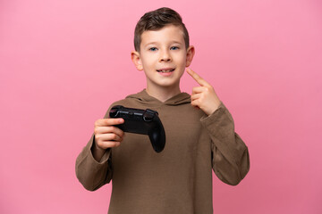 Wall Mural - Little caucasian boy playing with a video game controller isolated on pink background giving a thumbs up gesture