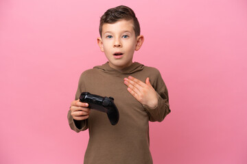 Wall Mural - Little caucasian boy playing with a video game controller isolated on pink background surprised and shocked while looking right