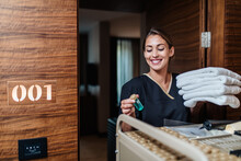 Beautiful Young Hotel Chambermaid In Uniform Bringing Clean Towels And Other Supplies To Hotel Room.