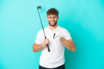 Young handsome caucasian man isolated on blue background playing golf and with thumbs up because something good has happened