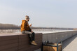 © satura_ - Bearded thoughtful man holds drink looking away while standing against river shore and sky background with copy space area for your text , attractive lonely male sits on city promenade background