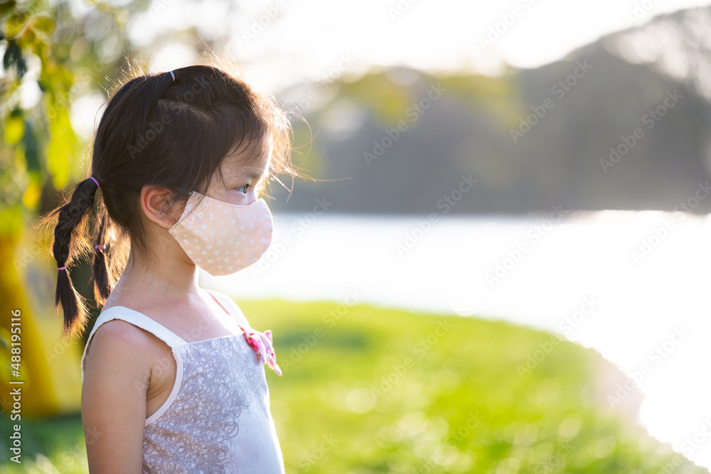 Side view of cute kid girl wearing cloth face mask was standing in park ...