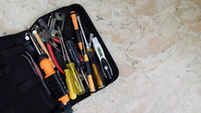 A Tool Bag With Unsorted Tools Of Tweezers, Screwdrivers, Pliers, And Others. Placed On A Marble Surface With Copy Space On The Right.