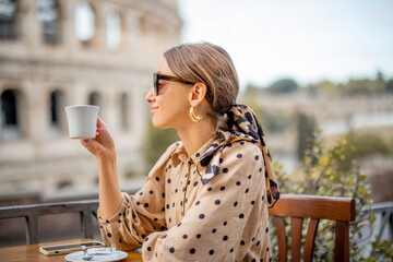 Wall Mural - Woman drinking coffee at outdoor cafe near coliseum, the most famous landmark in Rome. Concept of italian lifestyle and traveling Italy. Caucasian woman wearing dress and shawl in hair