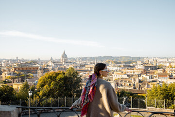 Wall Mural - Woman enjoying beautiful morning cityscape of Rome, walking in Villa Borghese Park. Old fashioned woman wearing coat with colorful shawl in hair. Concept of italian lifestyle and travel