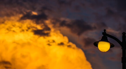 Wall Mural - Background of a bright colorful sunset with orange clouds and a yellow street lamp
