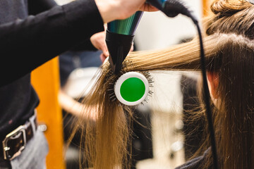 Canvas Print - Master woman hairdresser dries the girl's hair with a hairdryer and combs after washing in the beauty salon.