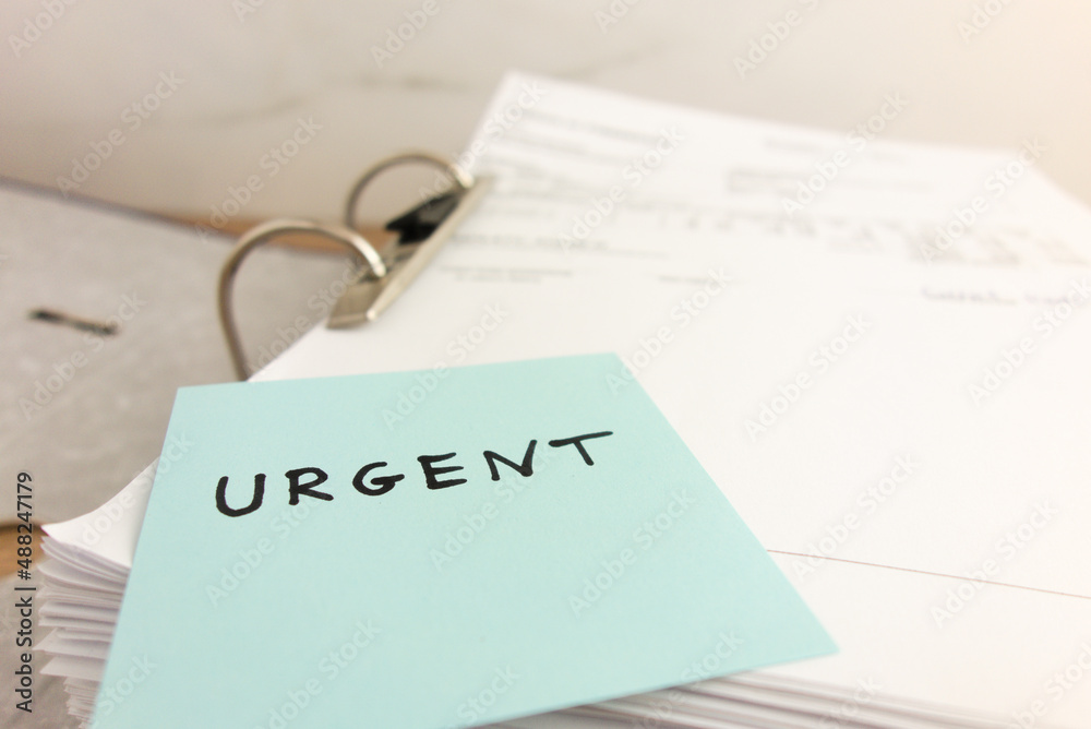 Sticky note with word urgent lying on stack of business paper files ...