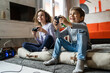 © Miljan Živković - Two children small caucasian brother and sister happy children siblings boy and girl playing video game console using joystick or controller while sitting at home real people family leisure concept