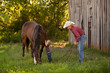 Child kissing horse with father standing nearby on pasture land near an old barn on a cattle ranch