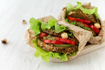 Vegan sandwiches of whole grain bread, tomatoes, peppers and avocados with spicy sauce and lettuce leaves wrapped in paper on a wooden tray. Close-up. Healthy food. Diet breakfast.