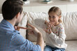 © fizkes - Happy pretty daughter kid and father talking with gestures, speaking sign language at home. Therapist training smiling child with hearing disability, deafness to use hands, fingers for communication