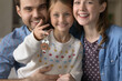 © fizkes - Happy millennial couple of parents and sweet daughter kid holding keys, showing house shape pendant, looking at camera, smiling. Family of homeowners, tenants buying home property, renting apartment
