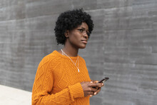 Young Afro Woman Holding A Mobile Phone While Walking On The Street. Technology And Urban Lifestyle Concept.