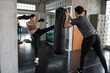 young woman kick boxing sandbag with trainer