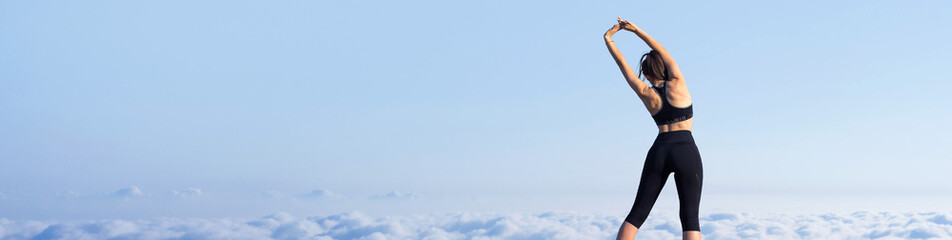 A young slim athletic girl in sportswear performs a set of exercises. Fitness and healthy lifestyle  against the background of clouds sky.