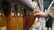 Woman enjoys shopping looking for fresh juice in supermarket. Hand of customer taking glass bottle with brown beverage at grocery department closeup