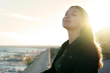 Pretty young woman with closed eyes breathing relaxing enjoying sun at sunset. Beauty sunshine girl side profile portrait. Positive emotion life success mind peace concept.