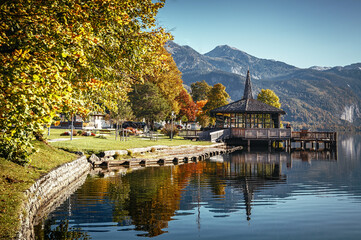 Fototapete - Colorful autumn landscape in the mountains with yellow Trees and lake glowing by sun and high mountain peaks behind. Amazing calm Grundlsee lake. Austria. Concept of an ideal resting place and travel