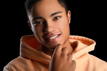 Poster - African-American teenage boy in hoodie smiling on black background, closeup