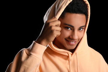 African-American teenage boy in hoodie smiling on black background, closeup