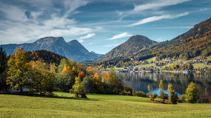 Fototapete - Scenic panorama of beautiful alpine autumn view with lake, mountains, green meadow and perfect sky. Amazing nature scenery. Wonderful sunny landscape. Grundlsee. Austria
