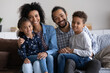 © fizkes - Portrait of smiling affectionate young African American couple parents holding on laps cute laughing little children siblings, happy friendly full family looking at camera, relations concept.