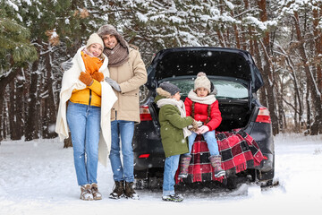 Poster - Happy family with thermos drinking hot tea near car in forest on snowy winter day