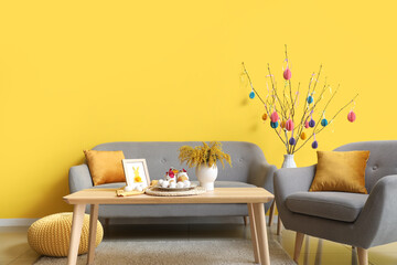 Easter cake, eggs and mimosa flowers on wooden table in living room interior