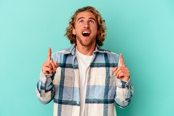 Wall Mural - Young caucasian man isolated on blue background pointing upside with opened mouth.