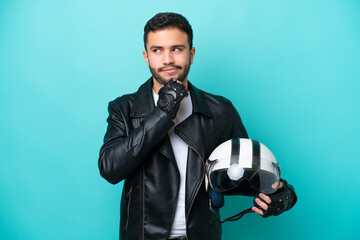 Wall Mural - Young Brazilian woman with a motorcycle helmet isolated on blue background having doubts and thinking