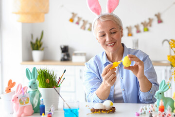 Wall Mural - Mature woman painting Easter eggs at home