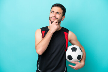 Wall Mural - Young football player Brazilian man isolated on blue background having doubts