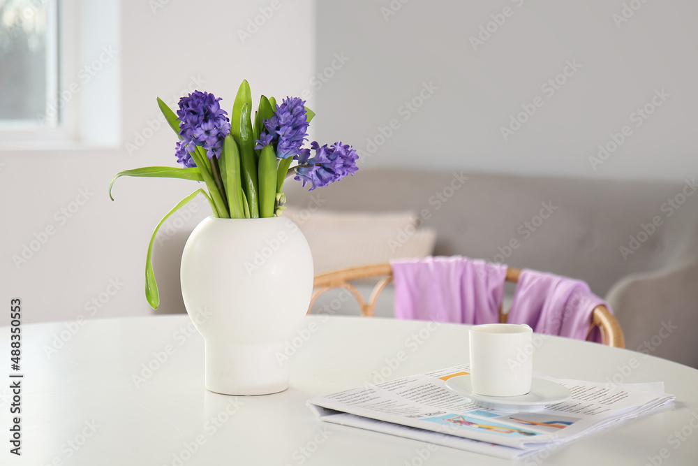 Newspaper, cup with coffee and vase with flowers on dining table in room